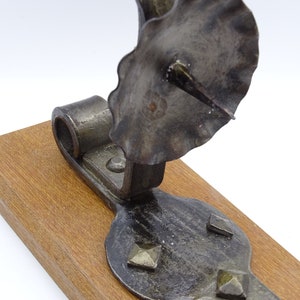 May include: A rustic, black metal candle holder with a scalloped top and a pointed spike for holding a candle. The holder is mounted on a wooden base.