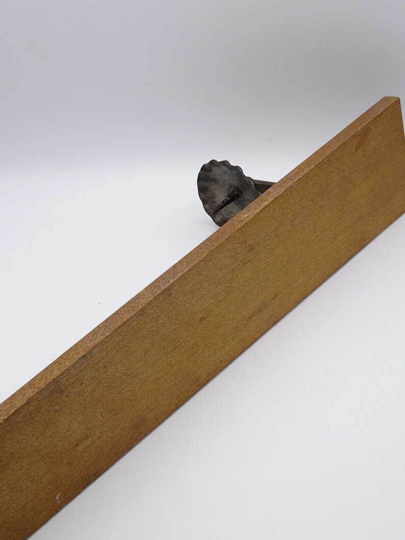 May include: A wooden shelf with a metal bracket in the shape of a seashell. The shelf is light brown and the bracket is dark gray.