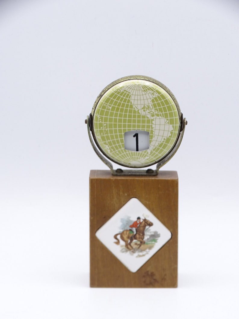 May include: A vintage wooden desk calendar with a green globe design and a white horse rider illustration. The calendar features a flip-up window displaying the number "1".