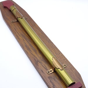 K&ouml;nnte beinhalten: Ein Messingteleskop, das auf einer Holztafel mit roten Holzendkappen montiert ist. Das Teleskop ist mit Messingklammern an der Tafel befestigt.