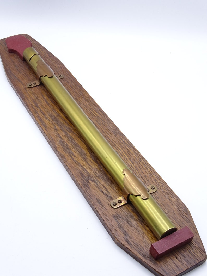 K&ouml;nnte beinhalten: Ein Messingteleskop, das auf einer Holztafel mit roten Holzendkappen montiert ist. Das Teleskop ist mit Messingklammern an der Tafel befestigt.