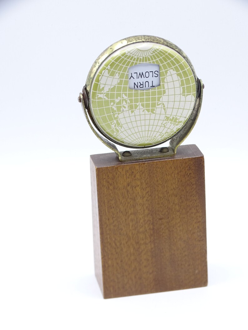 May include: A small, brass globe with a green map and a white label that reads "TURN SLOWLY". The globe is mounted on a wooden base.