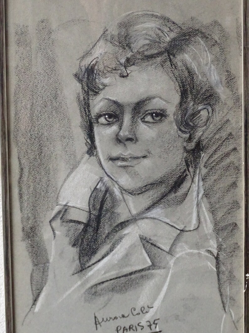 May include: Black and white charcoal drawing of a young person with short hair, wearing a collared shirt. The drawing is signed "Aurora Cec Paris 75".