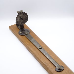 May include: A rustic metal candle holder with a circular base and a decorative, scalloped top. The holder is mounted on a wooden plank.