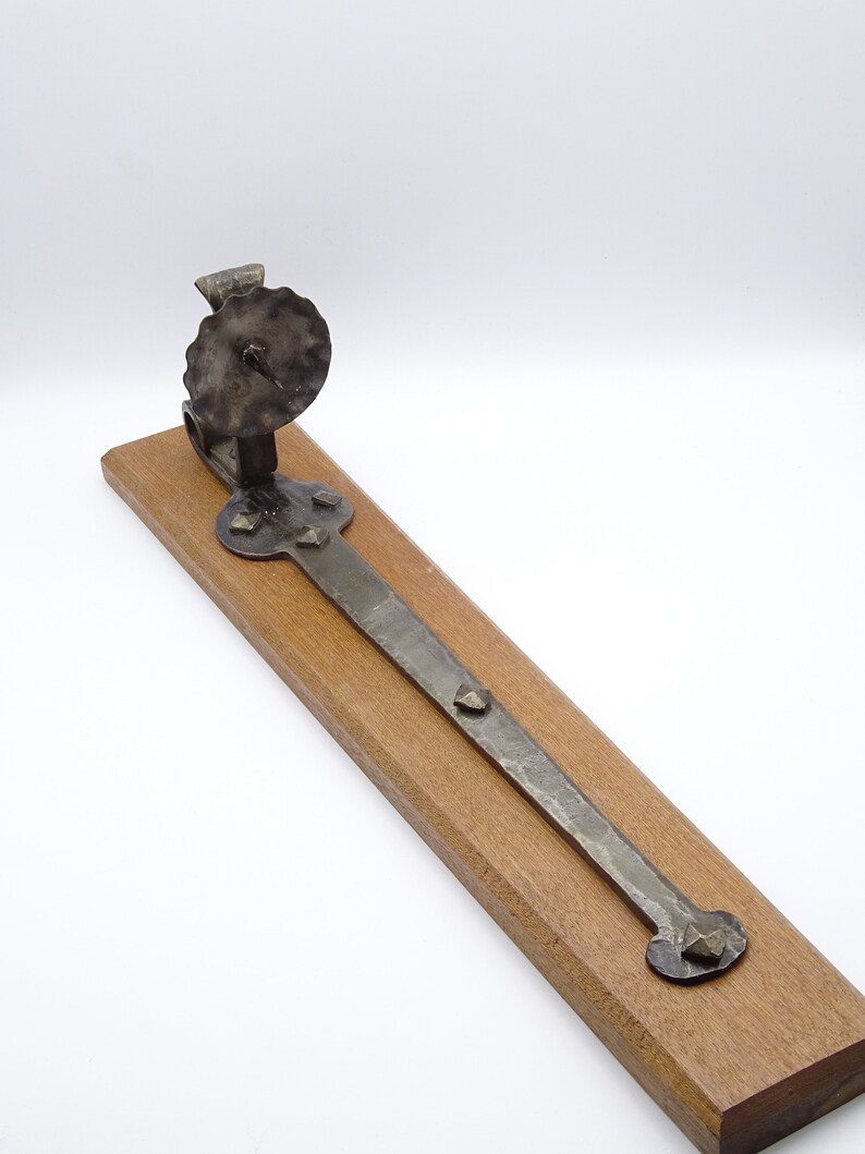 May include: A rustic metal candle holder with a circular base and a decorative, scalloped top. The holder is mounted on a wooden plank.