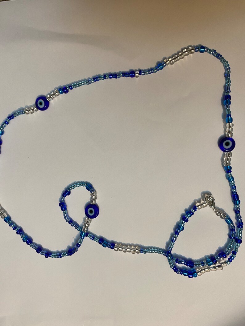 以下が含まれることがあります： 青と白のビーズと青い邪眼チャームが付いたビーズネックレス2本セット。ネックレスは長く、ブレスレットは短いです。