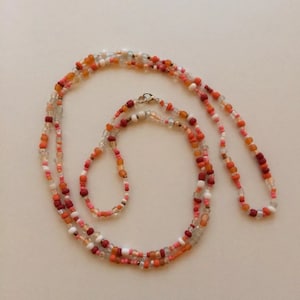 May include: A multi-strand beaded necklace featuring a blend of orange, red, white, and clear beads. The necklace is crafted from small, round beads and boasts a simple, elegant design.