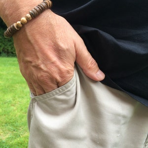 Op de afbeelding: Een bruine houten kralen armband op een mannen pols. De armband heeft gouden accenten en wordt gedragen op de linker pols.