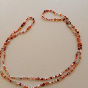 May include: A multi-strand necklace made of small, colourful beads in shades of red, orange, and white. The necklace is made of glass beads and has a silver clasp.