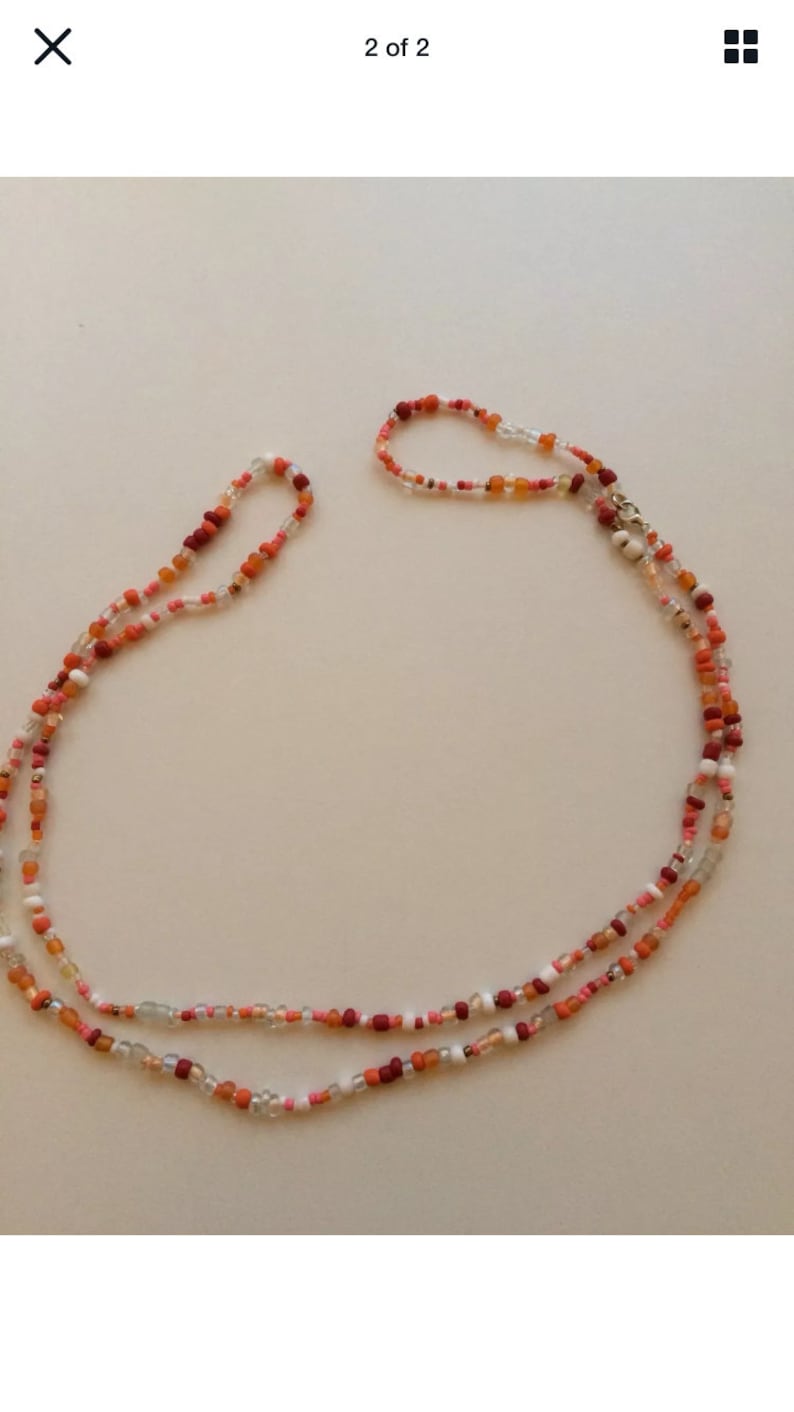 May include: A multi-strand necklace made of small, colourful beads in shades of red, orange, and white. The necklace is made of glass beads and has a silver clasp.