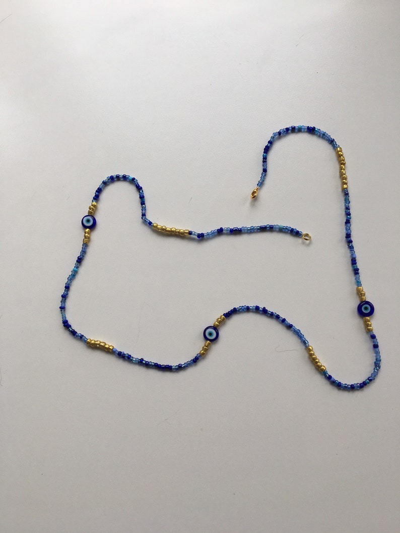 Pode incluir: Um colar de contas azuis e douradas com tr&ecirc;s pingentes de olho turco azul.