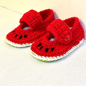 Puede incluir: Un par de zapatos de beb&eacute; de crochet rojo con un dise&ntilde;o de sand&iacute;a. Los zapatos tienen un borde blanco y un borde verde alrededor de la parte inferior.