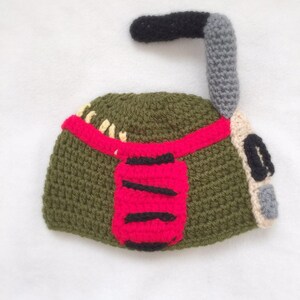 May include: Green, red, and gray crocheted hat shaped like a robot with a black antenna.
