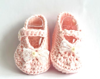 May include: A pair of pink crocheted baby booties with white lace bows and pearl accents.