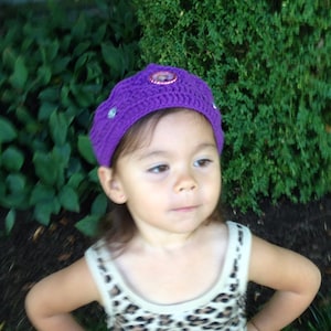 May include: A young girl wearing a purple crocheted crown with a sparkly jewel on top. She is wearing a leopard print tank top and has her hair pulled back.