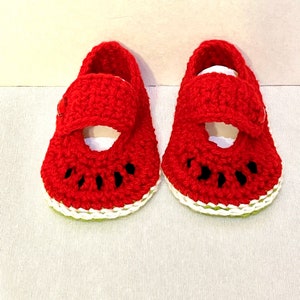Puede incluir: Un par de zapatos de beb&eacute; de ganchillo rojo con forma de rodajas de sand&iacute;a. Los zapatos tienen un borde blanco y semillas negras.