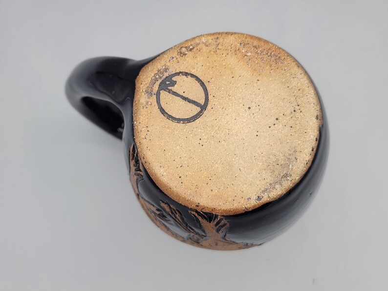Puede incluir: Taza de cer&aacute;mica negra con cuerpo redondeado y asa. La base de la taza no est&aacute; esmaltada, con un dise&ntilde;o estampado. La taza tiene un dise&ntilde;o floral tallado alrededor de la base.