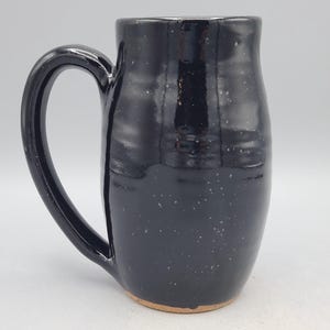Puede incluir: Una taza alta de cer&aacute;mica negra con un asa grande. La taza tiene un dise&ntilde;o moteado y un acabado brillante. La base de la taza no est&aacute; esmaltada. Esta taza hecha a mano es adecuada para caf&eacute;, t&eacute; u otras bebidas.