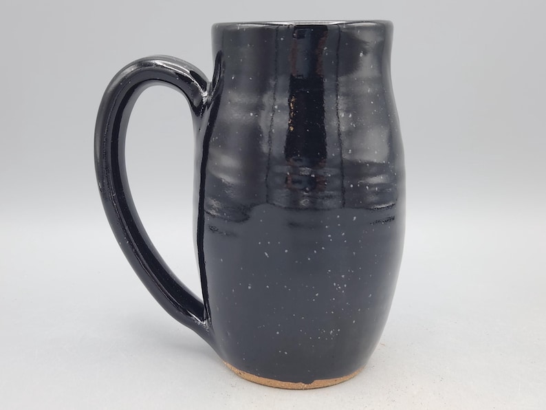 Puede incluir: Una taza alta de cer&aacute;mica negra con un asa grande. La taza tiene un dise&ntilde;o moteado y un acabado brillante. La base de la taza no est&aacute; esmaltada. Esta taza hecha a mano es adecuada para caf&eacute;, t&eacute; u otras bebidas.