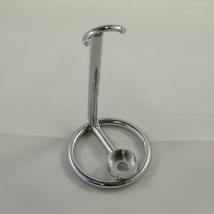 Puede incluir: Un soporte de afeitar cromado con una base circular y un brazo curvo para sujetar una navaja.