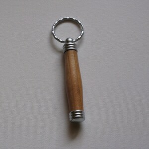 May include: A wooden keychain with a silver ring and silver accents. The keychain is brown and has a smooth finish.