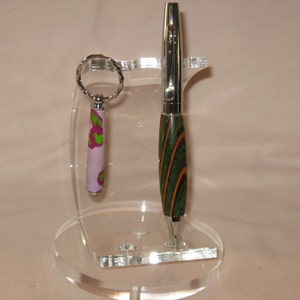 May include: A clear acrylic pen and keychain holder with a green and brown striped pen and a pink and green patterned keychain.