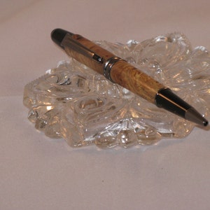 May include: A brown and black pen with a silver band on a clear glass surface.