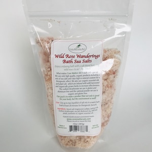 May include: A clear plastic bag of Wild Rose Wanderings Bath Sea Salts. The label includes the brand name, product name, and product details. The bag contains pinkish bath salts. The bag weighs 14oz (397g).