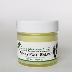 May include: A small, white jar with a yellow label. The label reads "CORE MATTERS SLC LOTIONS & POTIONS FOR ADVENTURERS FUNKY FOOT SALVE™ Anti-fungal, candida ointment NET WT 1 oz (28.3g)"