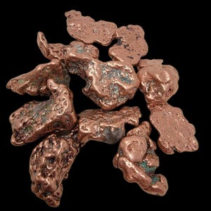 May include: A collection of raw copper nuggets, displaying a rich, reddish-brown hue with hints of green oxidation. The irregular shapes and textures of the copper pieces are set against a stark black background, highlighting their natural beauty. Ideal for collectors or jewelry makers.