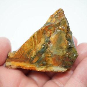 May include: A raw, triangular-shaped piece of jasper stone featuring a polished, glossy surface with a marbled pattern of earthy ochre, deep forest green, and burnt orange tones, showcasing natural mineral veins and a smooth, reflective texture.