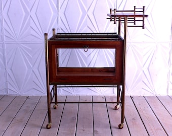 May include: A brass and wood bar cart with a glass shelf and a top shelf. The cart has four wheels and is on a wooden floor.