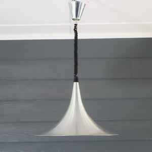 May include: A silver pendant light with a black cord hanging from a white ceiling. The light has a wide, funnel-shaped shade.