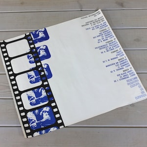 May include: A white poster with blue text and images. The poster advertises a film festival with the title "Festival Internacional del Cine". The poster features a film strip with images of a woman in a blue dress.