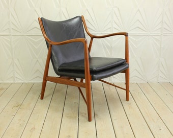 May include: A black leather armchair with a wooden frame. The chair has a simple, modern design with a low back and angled arms. The chair is sitting on a wooden floor.