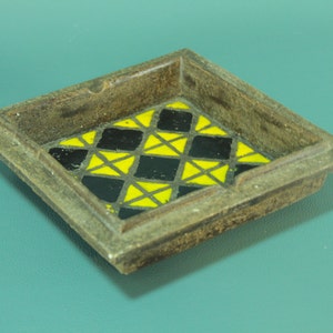 May include: A square ceramic ashtray with a geometric design of yellow and black triangles.