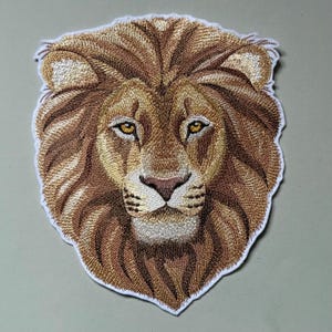 Könnte beinhalten: Gestickter Löwenkopf-Patch mit detailliertem Design. Der Löwe hat eine braune und goldene Mähne mit einem weißen Gesicht und einem ernsten Ausdruck. Der Patch ist perfekt, um Ihren Kleidungsstücken oder Accessoires einen Hauch von Wildheit zu verleihen.