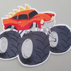 Könnte beinhalten: Ein roter Monstertruck mit großen schwarzen Reifen und orangefarbenen Flammen auf der Motorhaube. Der Truck hat einen weißen Umriss und ist gestickt.