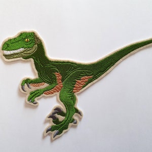 Könnte beinhalten: Grün gestickter Bügel-Patch mit einem Velociraptor-Dinosaurier mit orangefarbenen Akzenten.