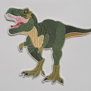Könnte beinhalten: Grüner gestickter Bügeleisen-Aufnäher mit einem Tyrannosaurus Rex Dinosaurier mit gelber Unterseite und roten Zähnen.
