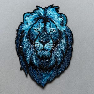 Könnte beinhalten: Blauer gestickter Löwenkopf-Patch mit Sternenhimmel-Design.