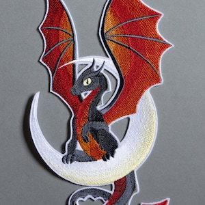 Könnte beinhalten: Gestickter Bügel-Patch mit einem schwarzen Drachen mit roten Flügeln und Schwanz, der auf einem weißen Halbmond sitzt.