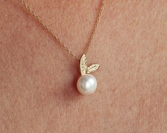 May include: A gold chain necklace with a pearl pendant and two small gold leaves.
