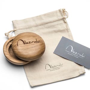 May include: A wooden jewelry box with a lid, open to reveal the interior. The box is next to a drawstring bag and a gray business card. The text "Alezraki" is engraved on the box and printed on the bag and card.