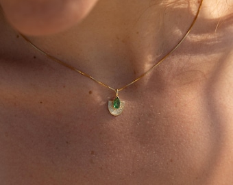 May include: A gold necklace with a pendant featuring a green gemstone and a half-circle design. The pendant is suspended from a delicate gold chain. The necklace is worn on a person's neck.