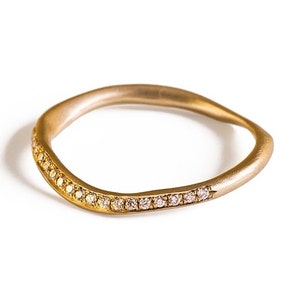 May include: A gold-toned ring with a wavy design. The ring is adorned with small, sparkling gemstones set along one side. The ring's smooth, polished surface contrasts with the glittering stones, creating a sophisticated look.