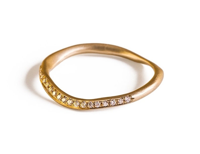 May include: A gold-toned ring with a wavy design. The ring is adorned with small, sparkling gemstones set along one side. The ring's smooth, polished surface contrasts with the glittering stones, creating a sophisticated look.