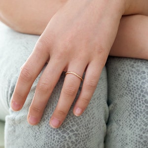 May include: A delicate gold ring with a curved design, set with small, sparkling stones. The ring is shown on a hand, highlighting its elegant and minimalist style. This ring is a perfect accessory for everyday wear or special occasions.