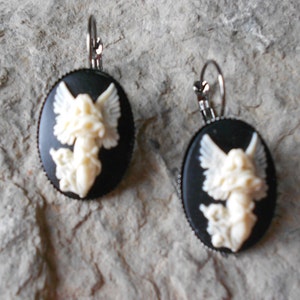 Puede incluir: Un par de pendientes de camafeo blanco y negro con un dise&ntilde;o de &aacute;ngel blanco. Los pendientes tienen ganchos plateados.