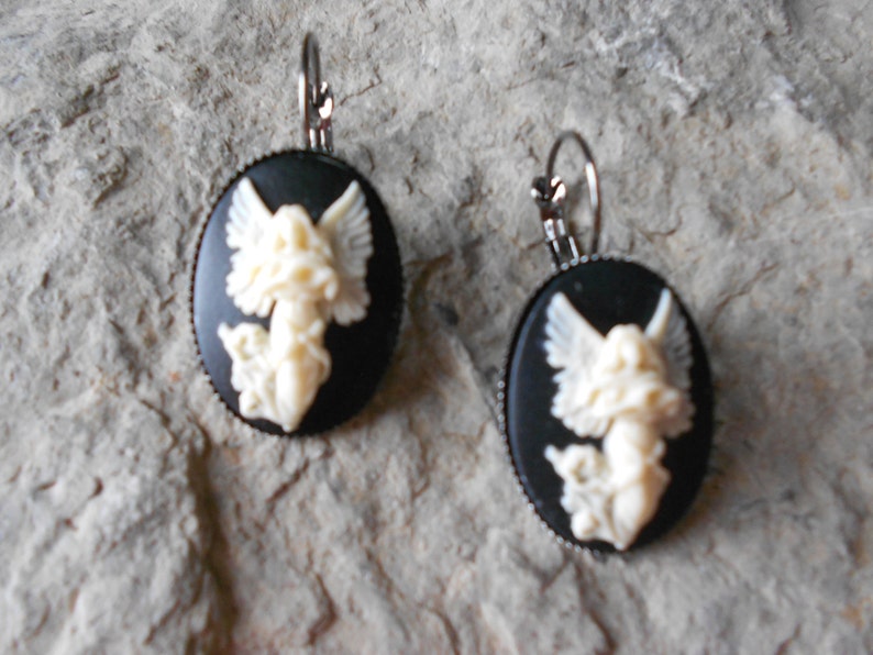 Puede incluir: Un par de pendientes de camafeo blanco y negro con un dise&ntilde;o de &aacute;ngel blanco. Los pendientes tienen ganchos plateados.